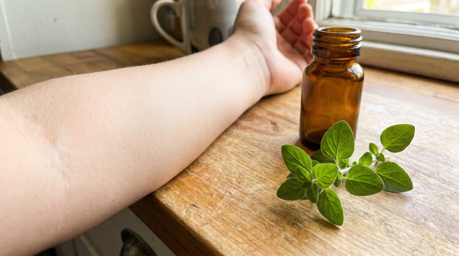 Calm clear forearm on a kitchen counter next to a small unlabeled bottle and a sprig of oregano