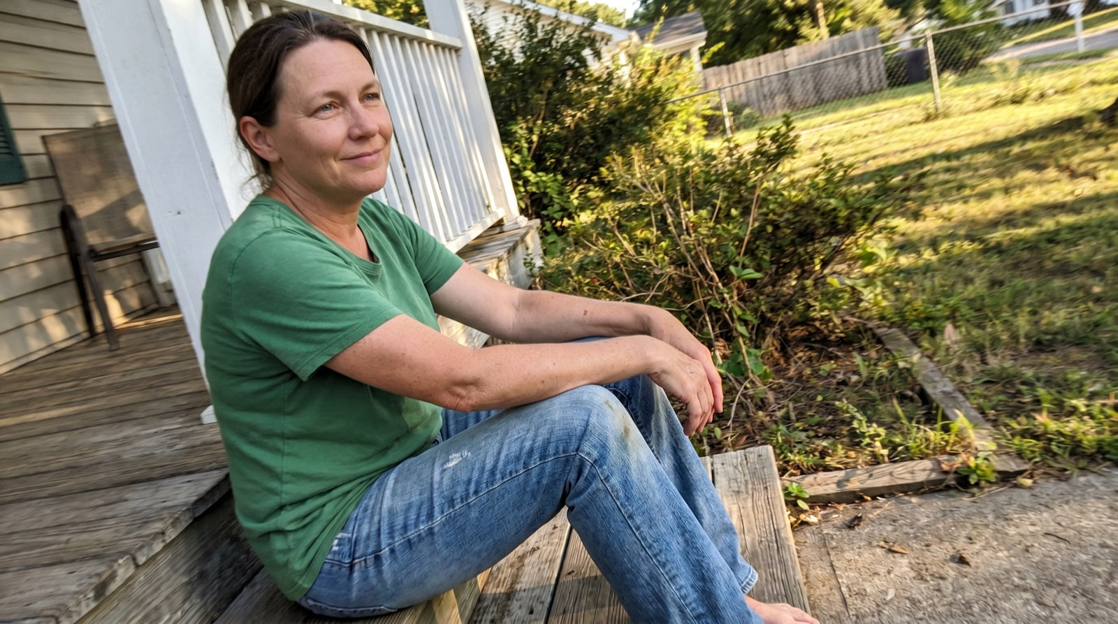 A woman sitting on her front porch in late afternoon sun, relaxed and content