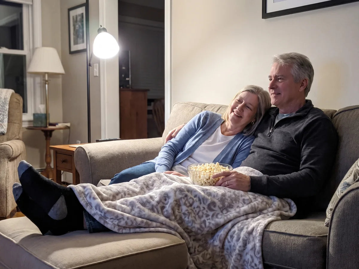 Michelle and her husband on the couch watching a movie, her legs resting still under a blanket