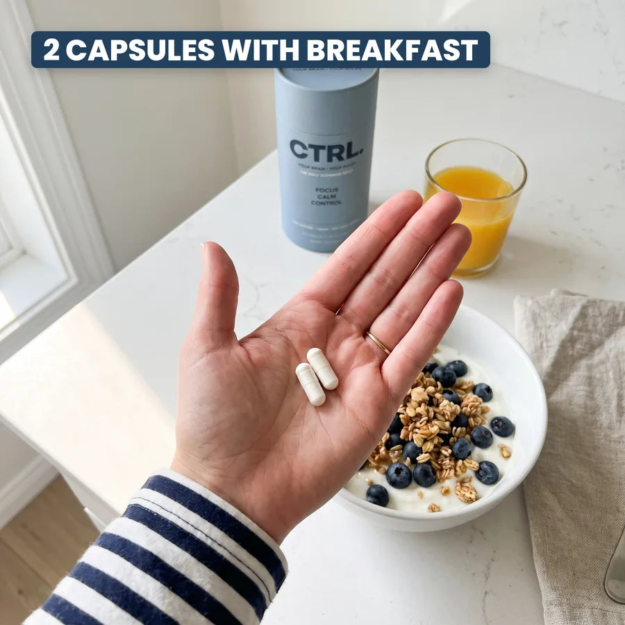 A hand holding two CTRL capsules over breakfast, the CTRL tube on the counter