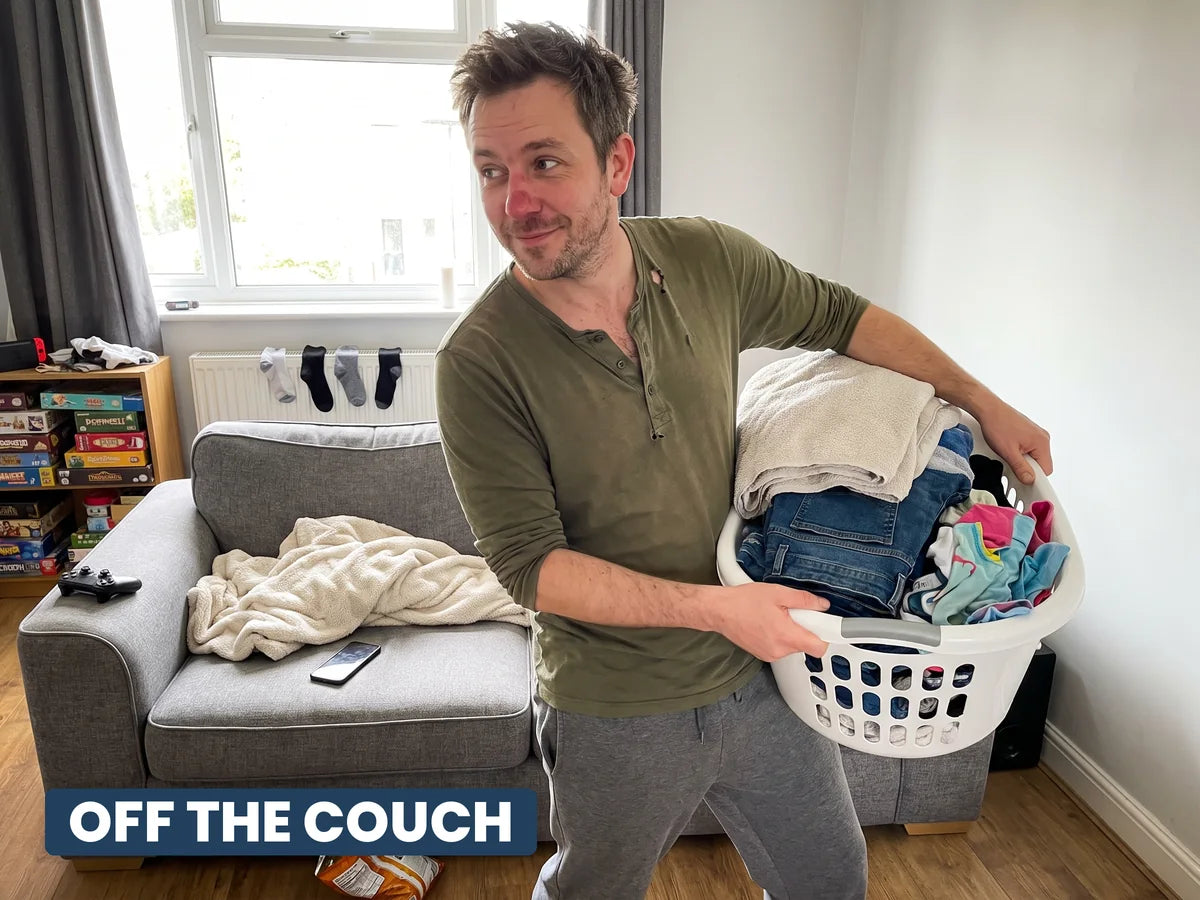 A man carrying a full laundry basket past the empty sofa, off the couch
