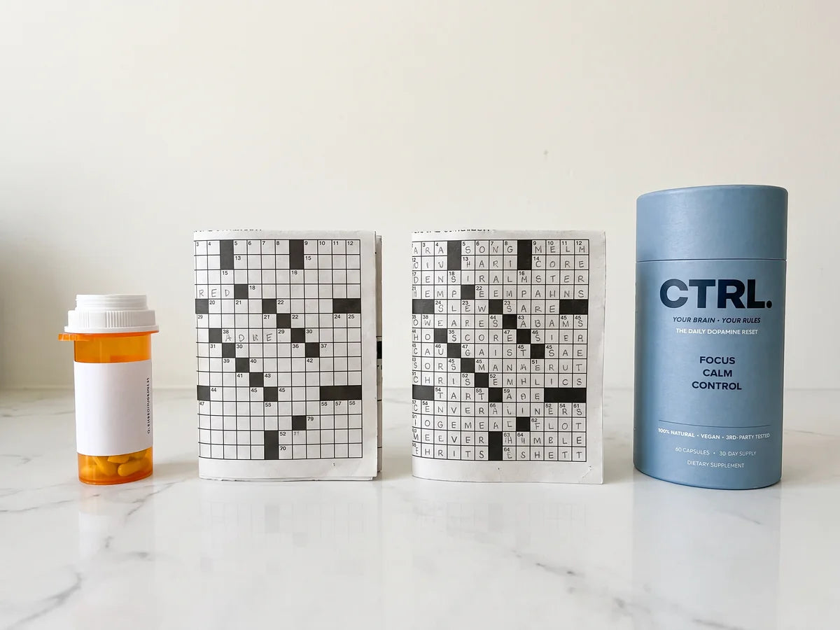 A prescription bottle next to two crosswords, one barely started and one finished, and a CTRL tube