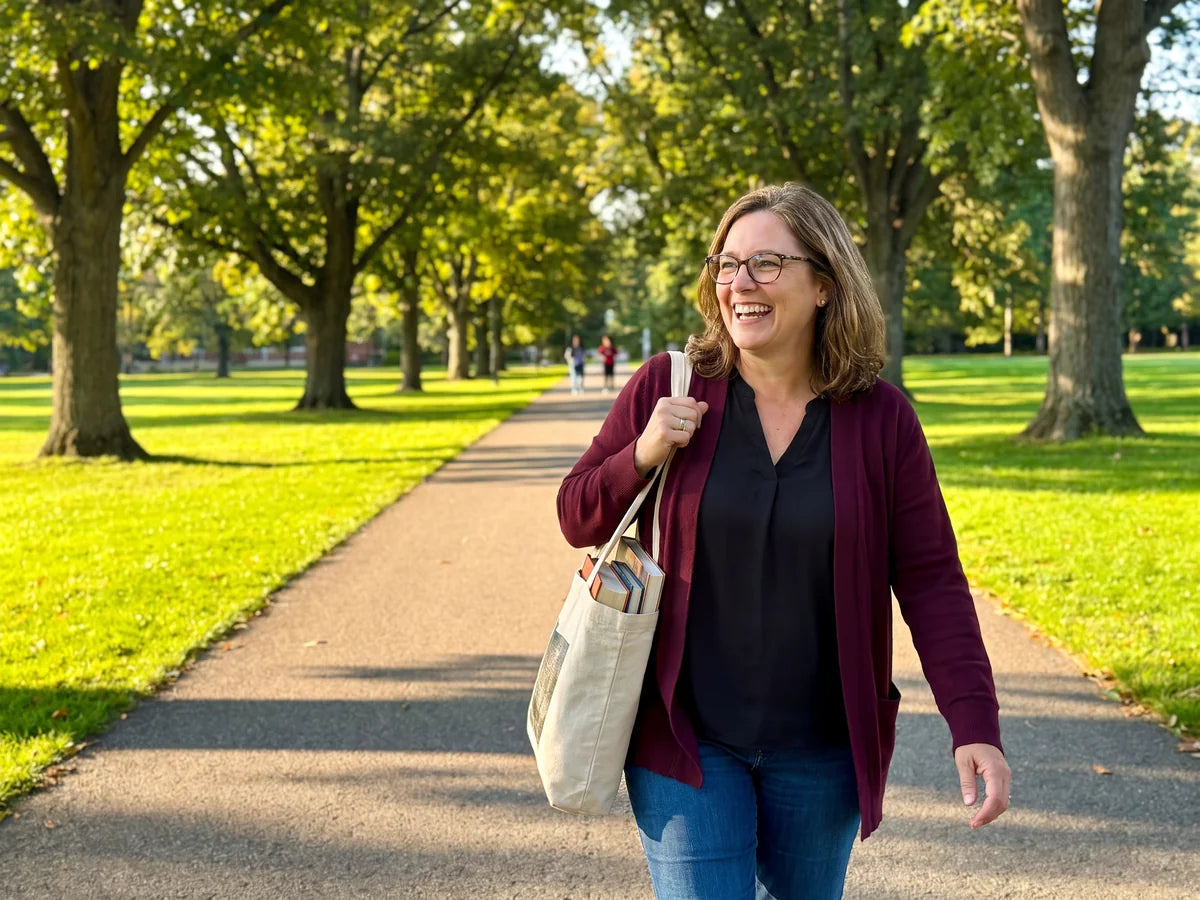 Linda walking across a sunny school campus with a tote bag of books, smiling