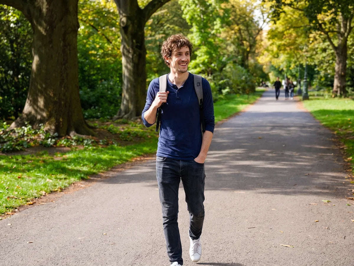 Jake walking through a park in the late afternoon, relaxed and smiling