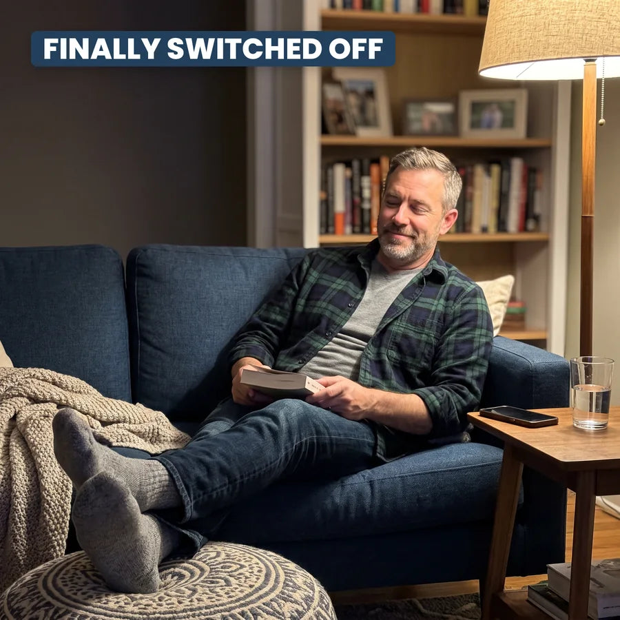 A man relaxed on his sofa in the evening with a book, phone face down